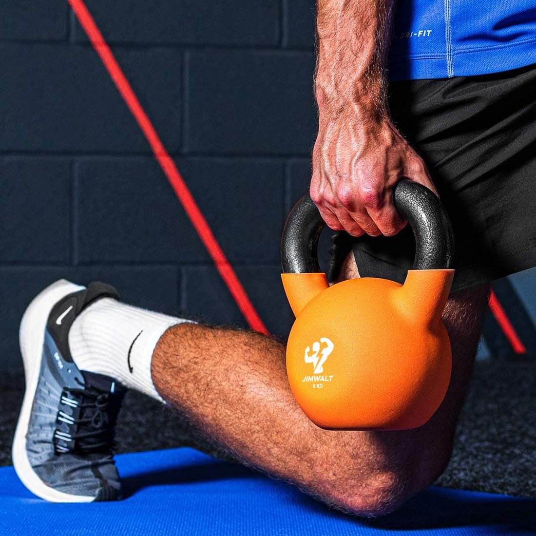 A man  is  holding an orange kettlebell in one hand.