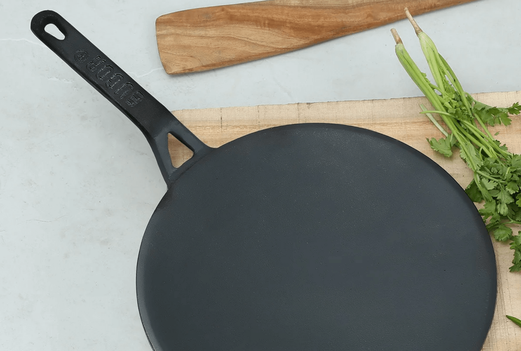 A black, circular cast iron tawa with a long handle