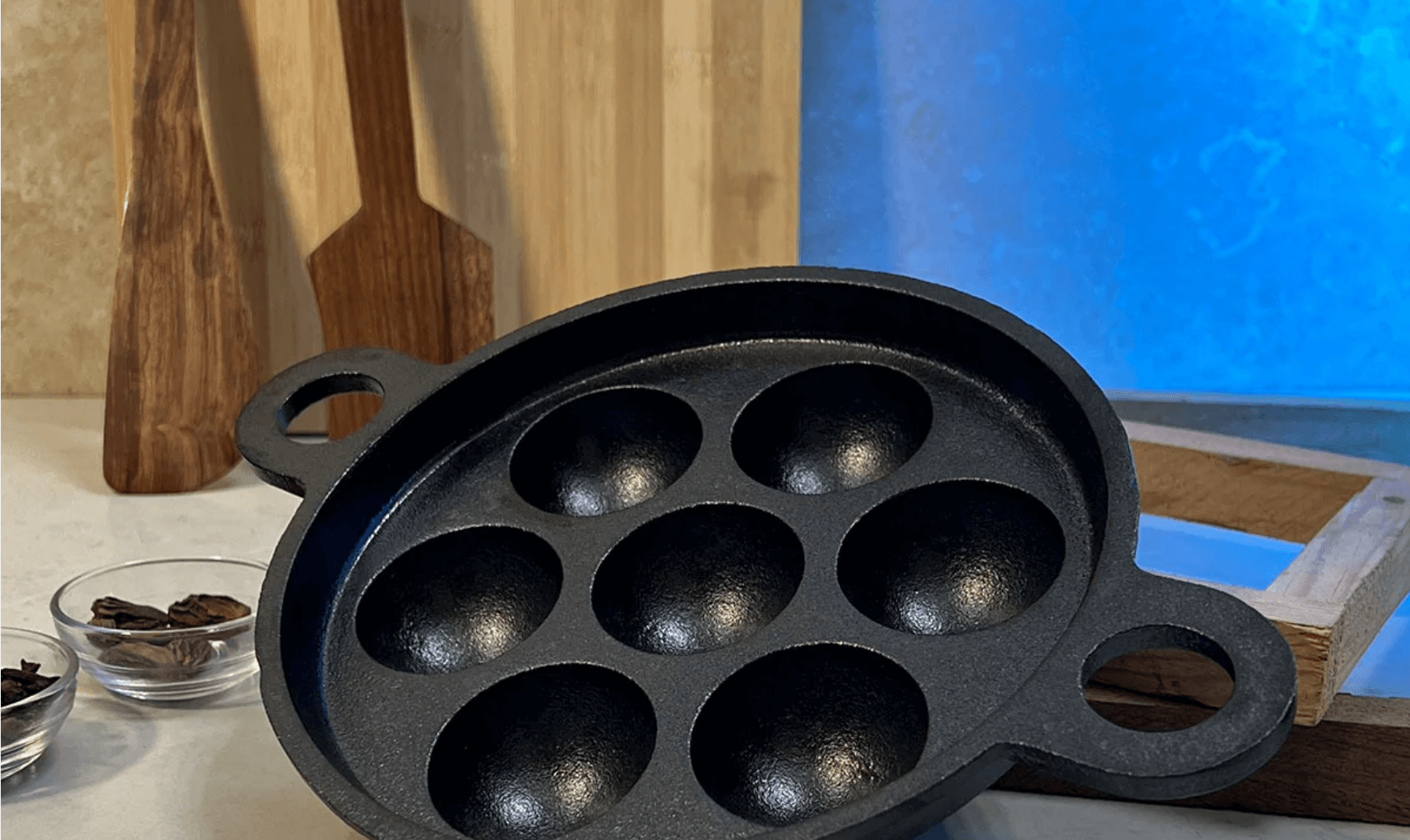 A black cast iron paniyaram pan with seven round depressions