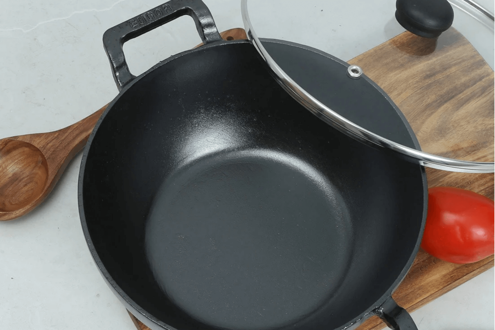 A black cast iron kadai with a glass lid.